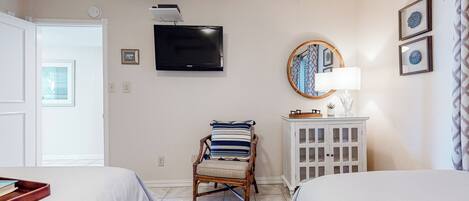 A bedroom with two beds, a television, a chair with a striped cushion, a cabinet, and a window with a view.