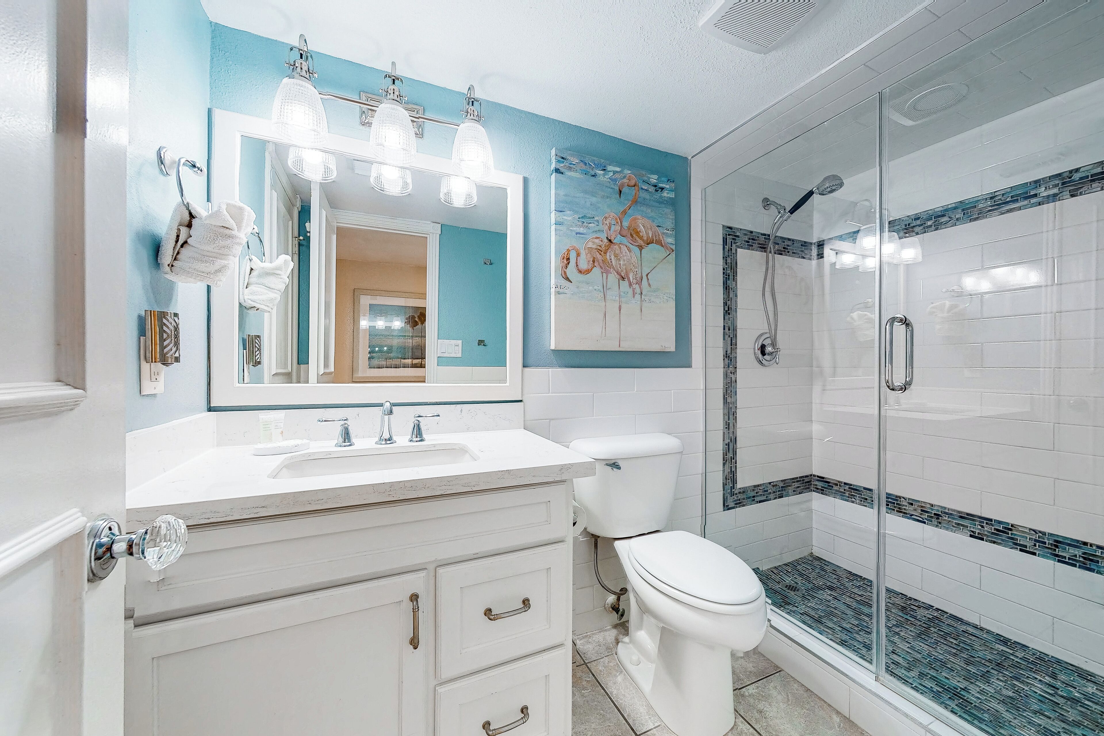 A bathroom with a white vanity, a large mirror, a toilet, and a glass-enclosed shower.