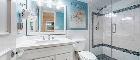 A bathroom with a white vanity, a large mirror, a toilet, and a glass-enclosed shower.