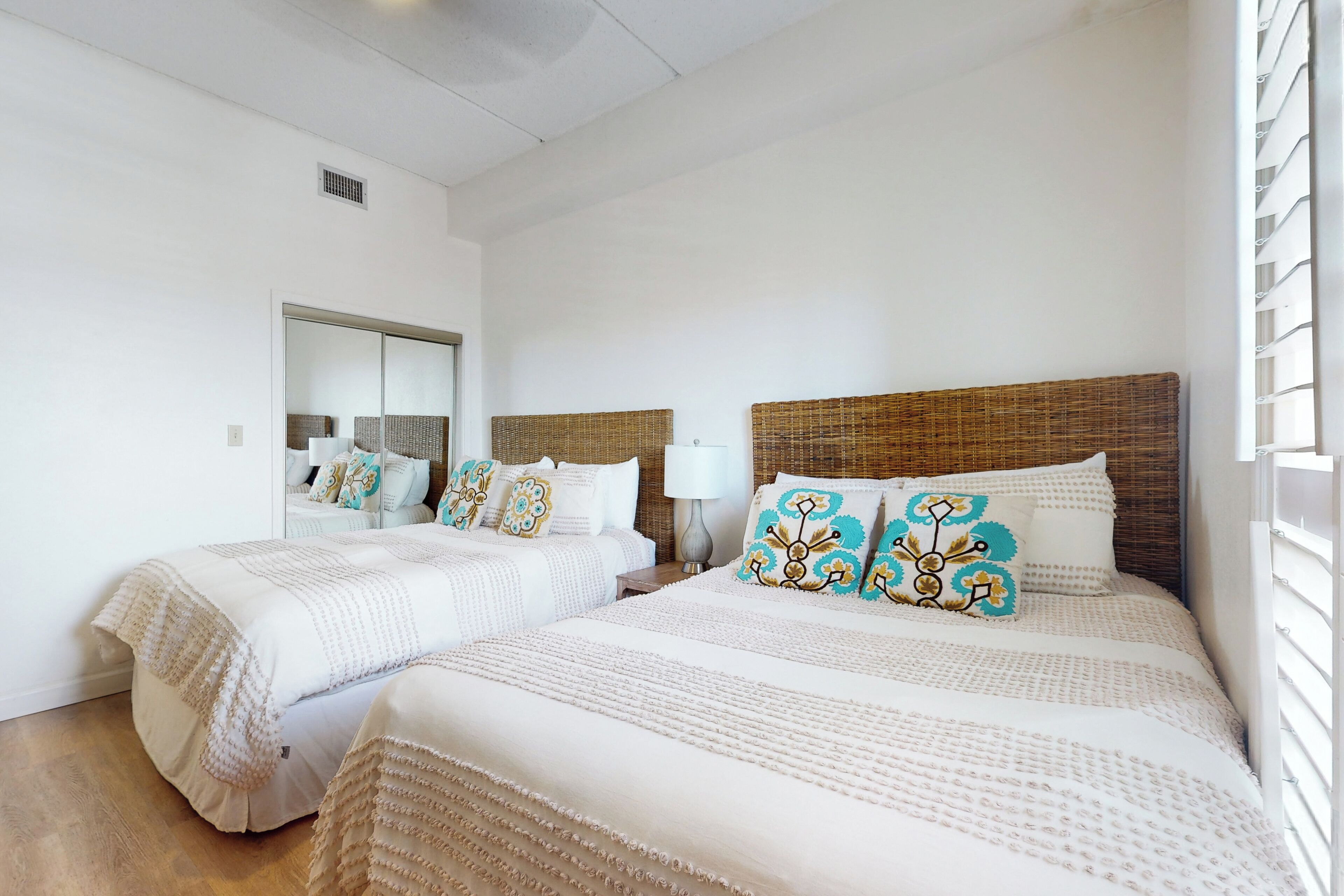 A hotel room with two beds, a large mirror, and a window with blinds.