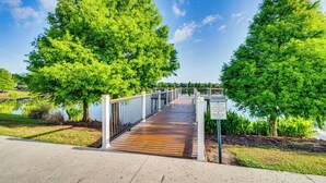 Un pont en bois enjambant une étendue d’eau, entouré d’arbres verdoyants et sous un ciel dégagé.