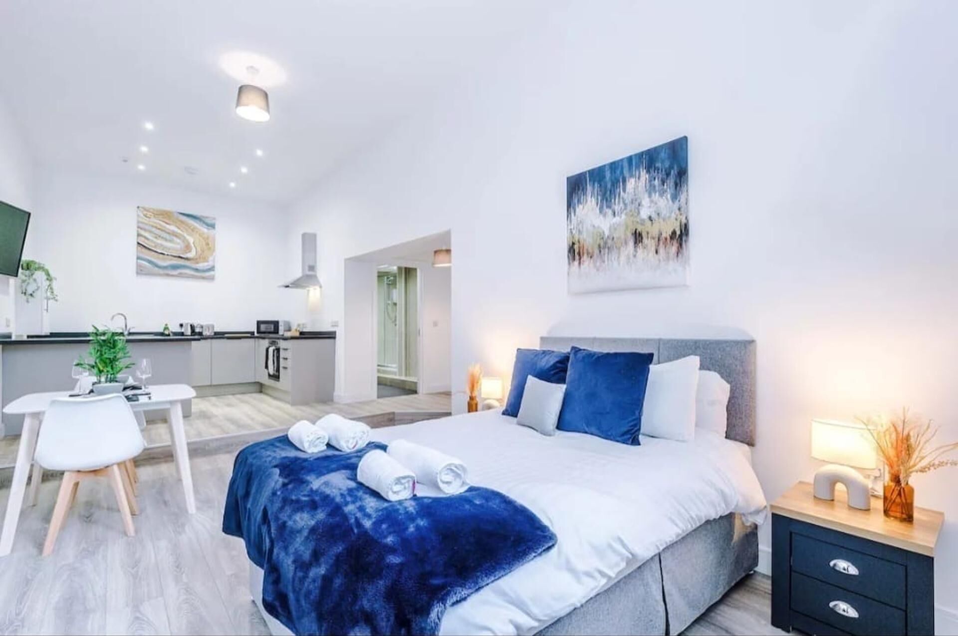 A modern bedroom with a large bed, a bedside table, a nightstand, and a painting on the wall.