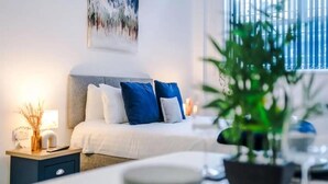 A modern bedroom with a bed, bedside table, lamp, and a potted plant. - Bolton City Oasis - Cozy Apartment Rental (Bolton)