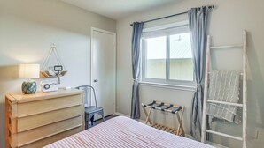Ein Schlafzimmer mit Bett, Kommode, Radio, Stuhl, Fenster mit Vorhängen und einer Wäscheständer.