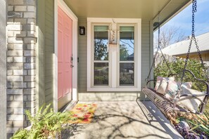 A porch with a bench, a pink door, and a window with a hanging light fixture. - Cowboy Pool & Fenced Yard: Convenient Austin Home (Austin)