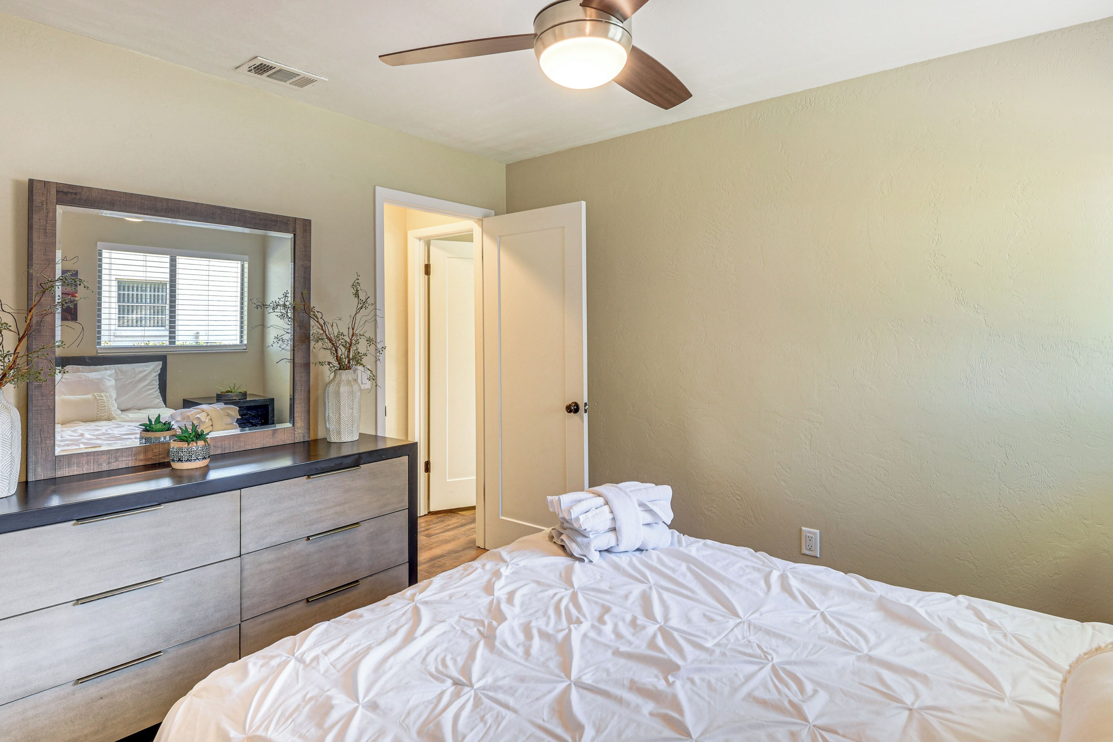 A bedroom with a bed, a dresser, a mirror, and a ceiling fan.