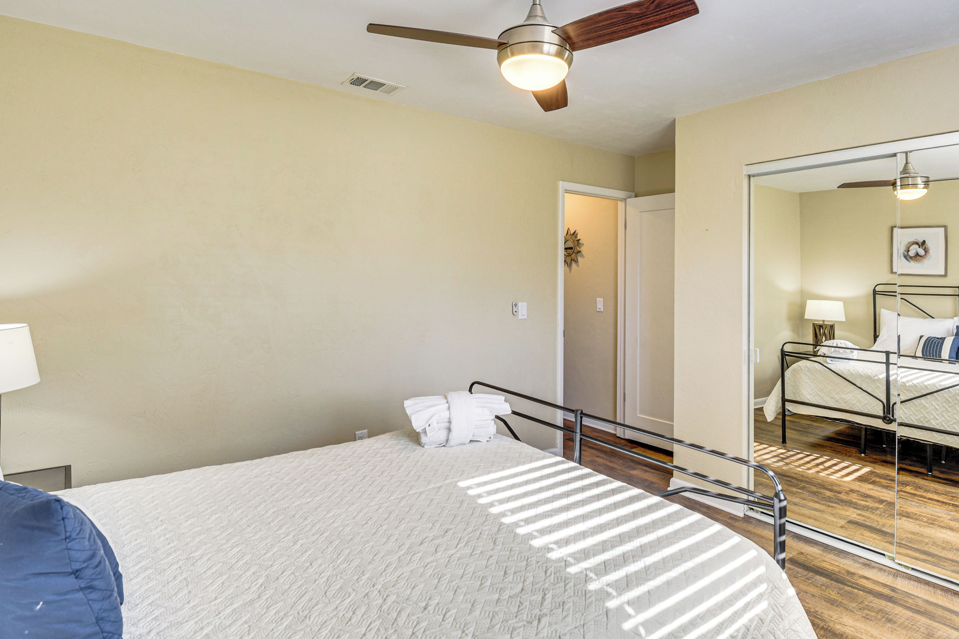 Un dormitorio con cama, ventilador de techo, espejo y puerta que da a otra habitación.