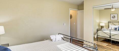 Un dormitorio con cama, ventilador de techo, espejo y puerta que da a otra habitación.