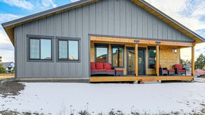 En moderne hytte med en overdækket veranda, store vinduer og et snedækket terræn.