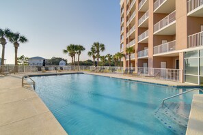 A swimming pool with lounge chairs and a building with balconies. - Ocean View, Walk to Beach: Gulf Shores Condo (Gulf Shores)