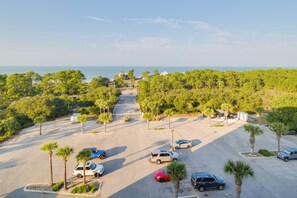 A parking lot with several cars, surrounded by trees and a view of the ocean. - Ocean View, Walk to Beach: Gulf Shores Condo (Gulf Shores)