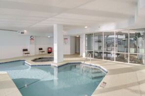 An indoor swimming pool with a hot tub, seating area, and a glass wall with exercise equipment. - Ocean View, Walk to Beach: Gulf Shores Condo (Gulf Shores)