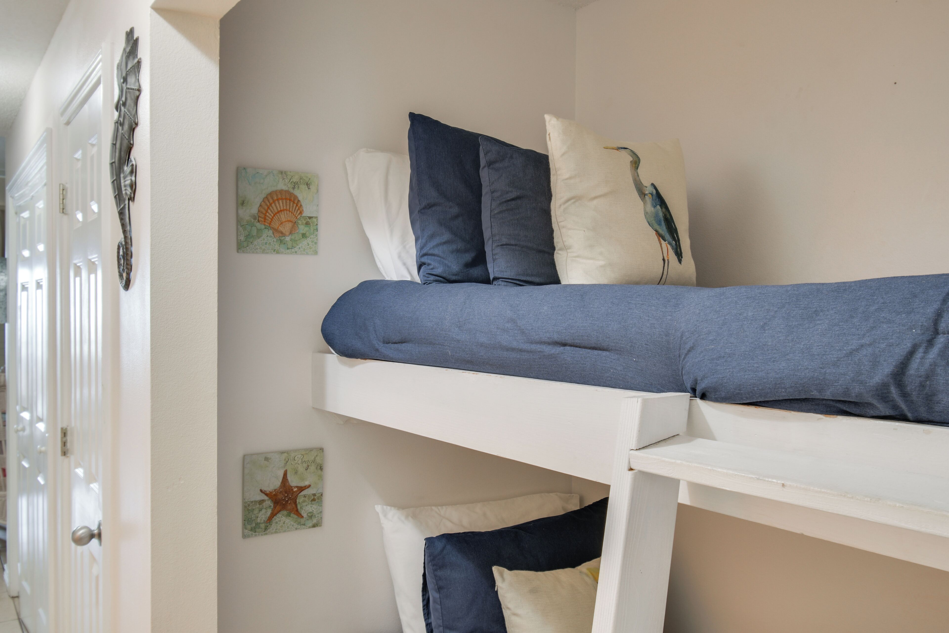 A bunk bed with pillows and wall art in a room with white walls and a door.