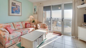 Ein Wohnzimmer mit einer Couch, einem Couchtisch und einem TV-Schrank. Eine Glastür führt zu einem Balkon.