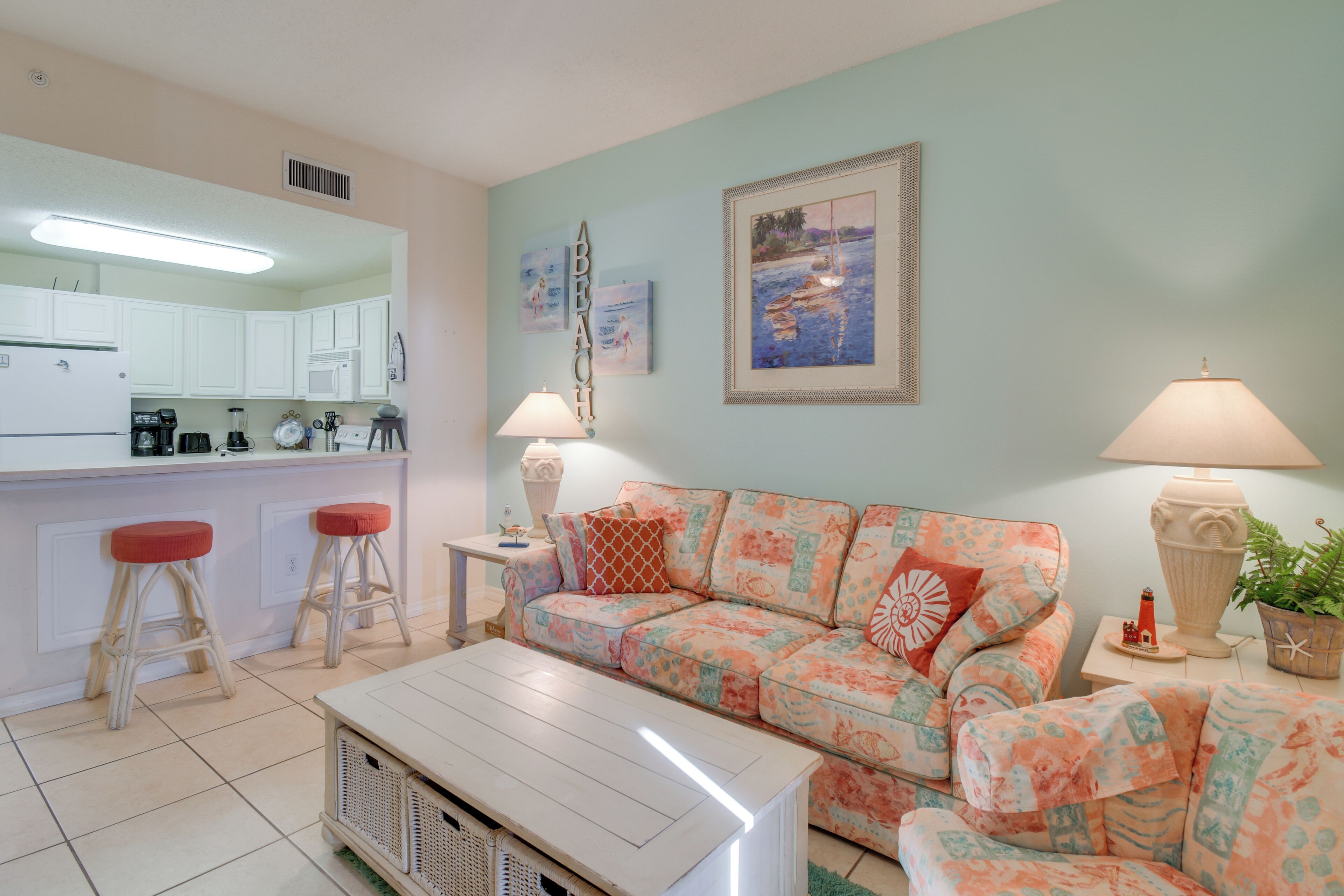 A living room with a sofa, a coffee table, and a kitchen area with white cabinets and a refrigerator.