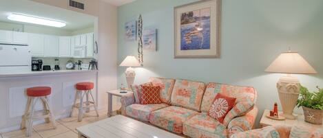 A living room with a sofa, a coffee table, and a kitchen area with white cabinets and a refrigerator.