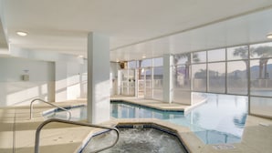 Ein Hallenbad mit klarem Wasser, einer Whirlpool und Blick auf Palmen durch große Fenster.
