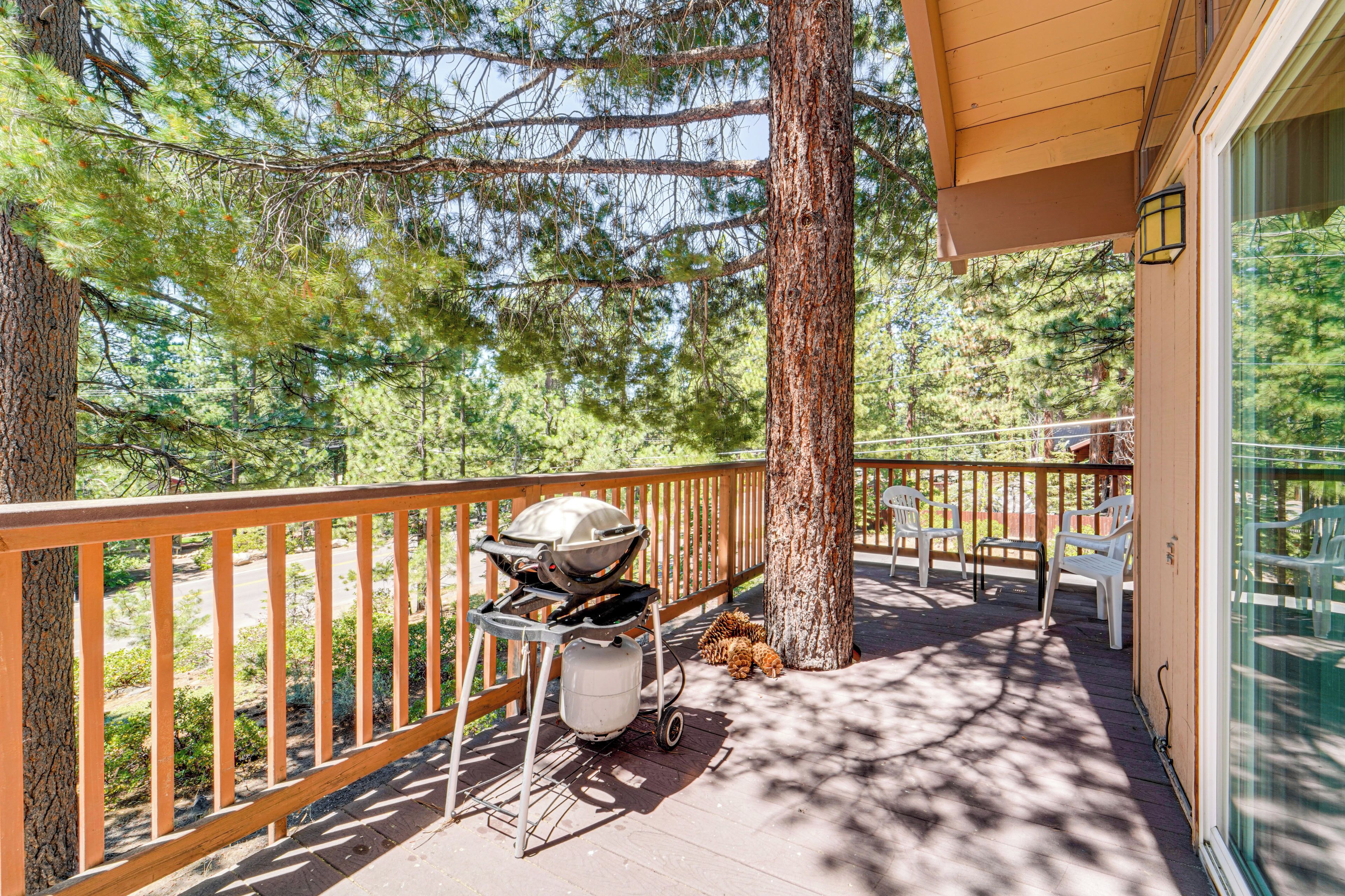 Une terrasse en bois avec un barbecue, des chaises blanches et une porte vitrée donnant sur un espace abrité.