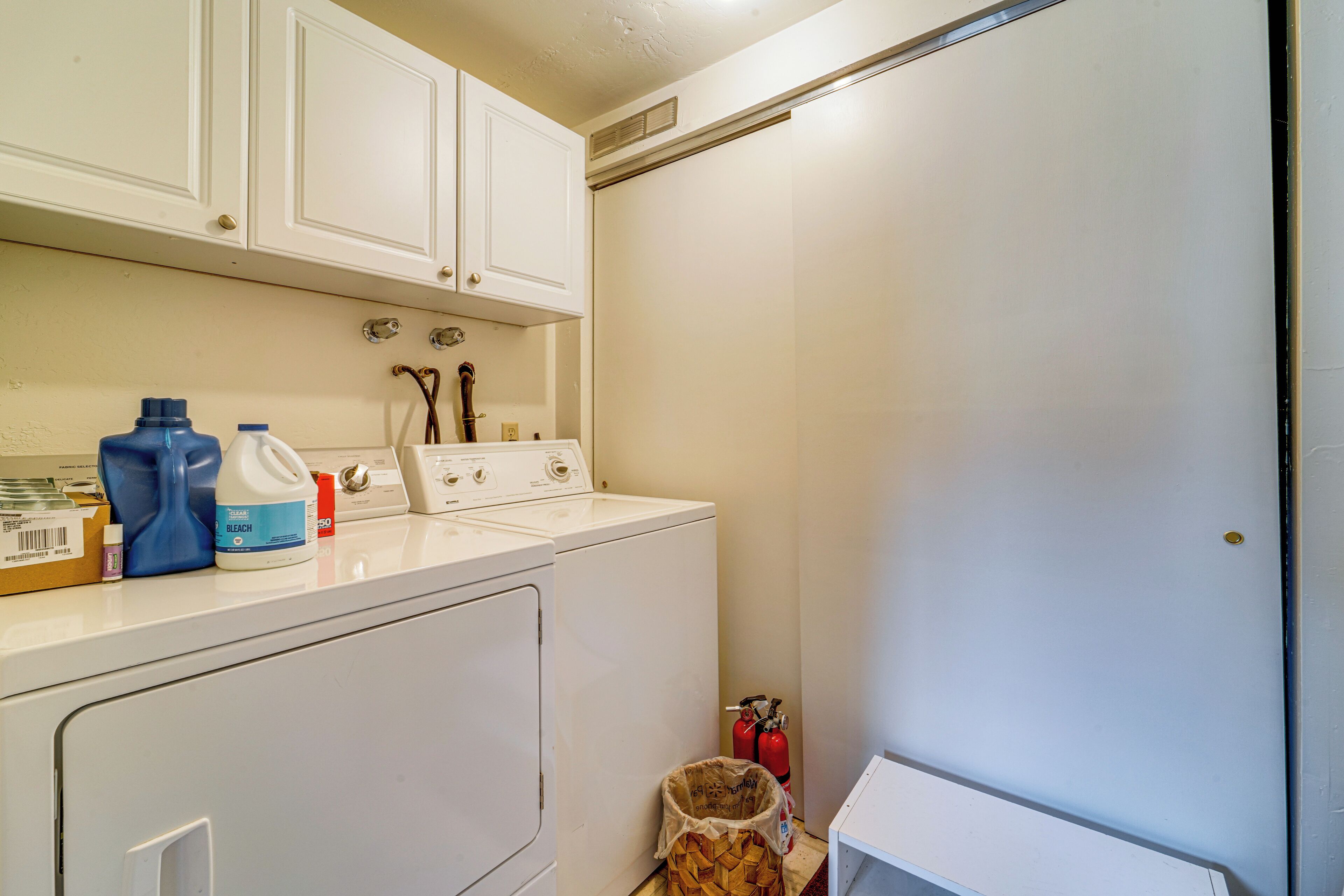 A laundry room with a washer and dryer, a fire extinguisher, and cleaning supplies on the counter.