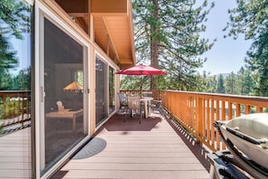 A wooden deck with a glass door leading to a room, a red umbrella, and a kayak.