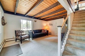 A living room with a wooden ceiling, a staircase, a sofa, and a chair.