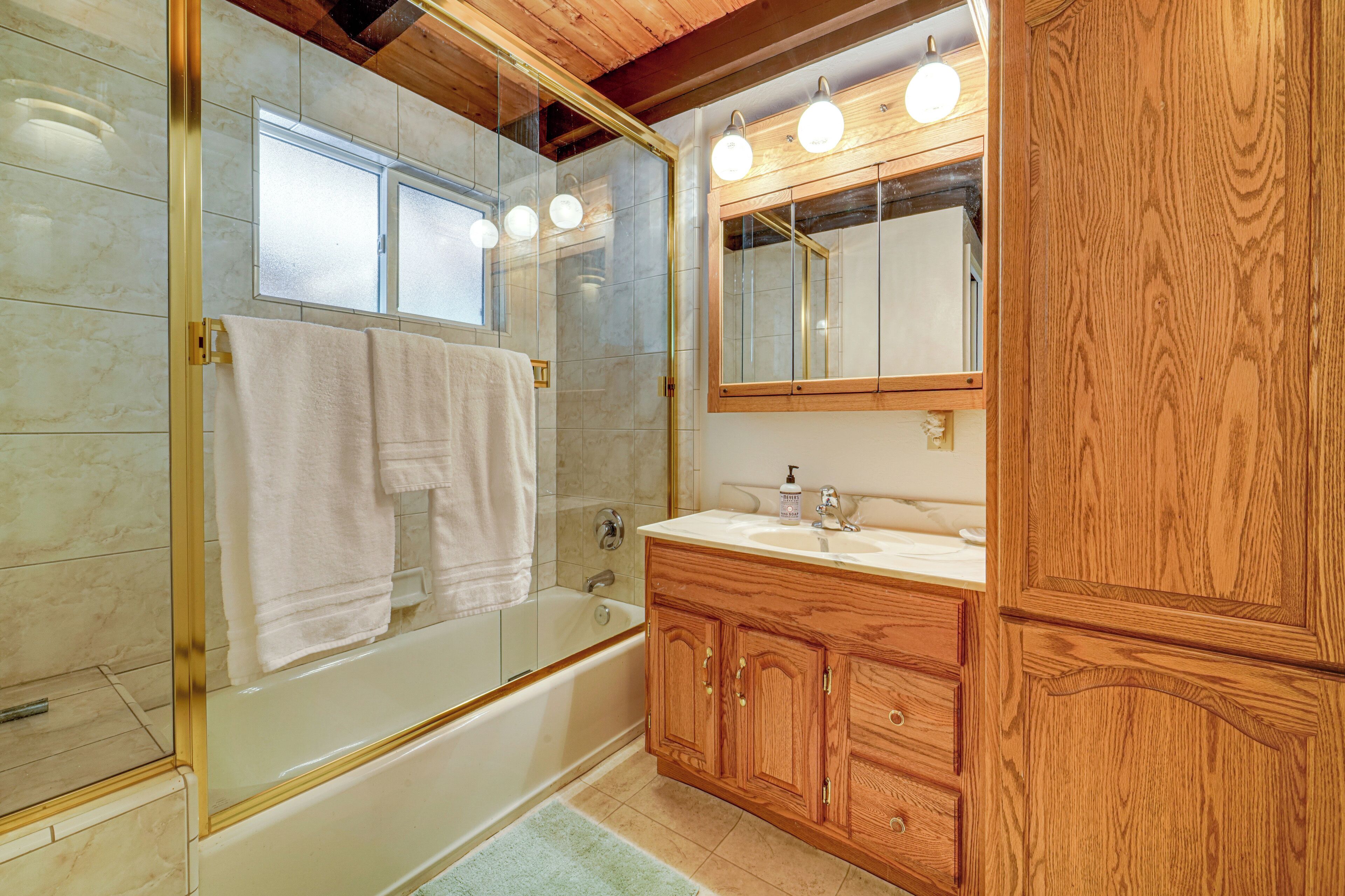 Un baño con ducha de vidrio, tocador de madera con espejo y bañera.