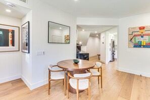 Un espace de repas moderne avec une table ronde en bois et quatre chaises, une cuisine en arrière-plan et des œuvres d’art accrochées aux murs.
