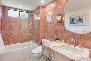 Un baño con bañera, inodoro y lavabo, con pared de azulejos y un espejo grande.