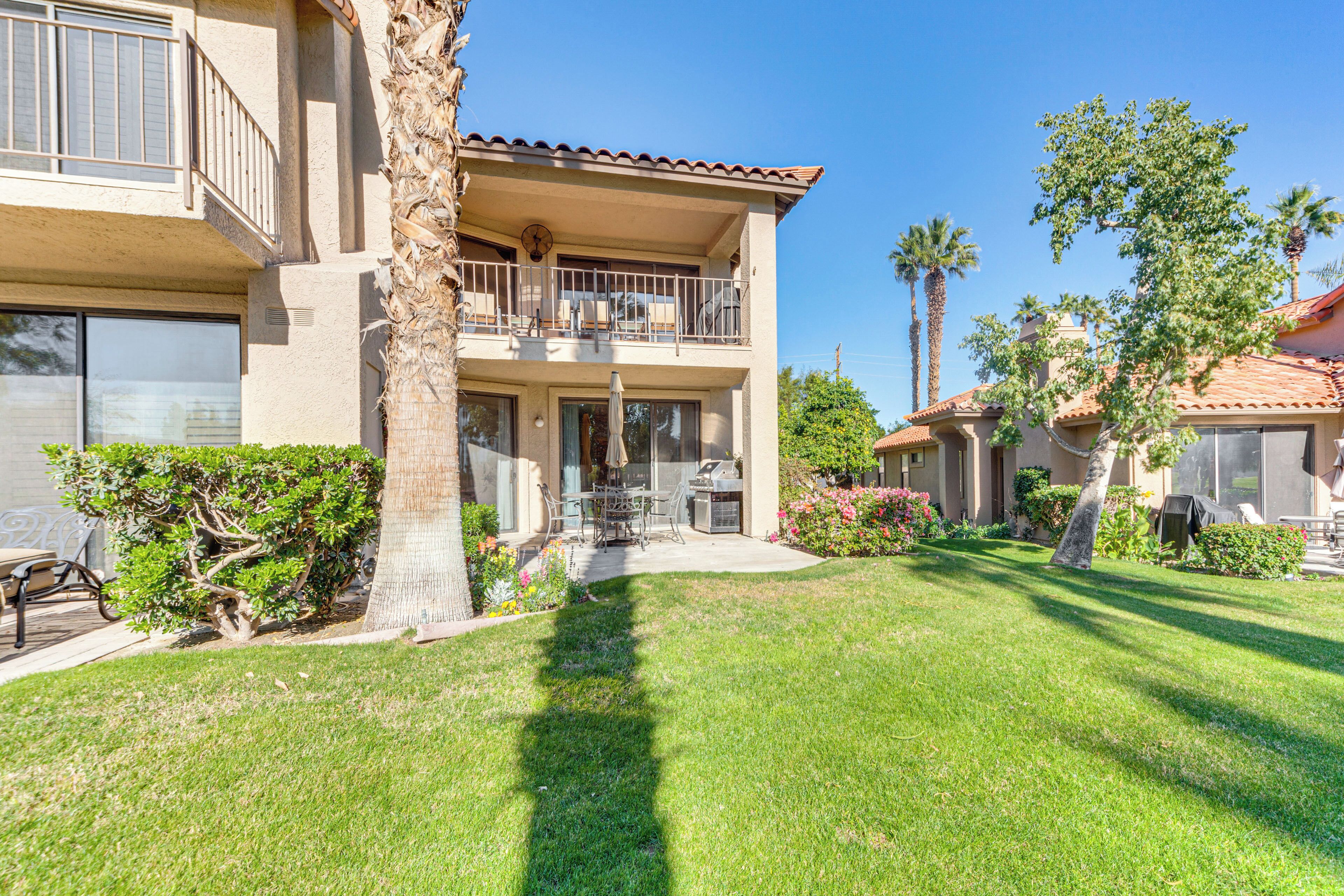 A two-story building with a balcony, a patio with outdoor furniture, and a well-maintained lawn.