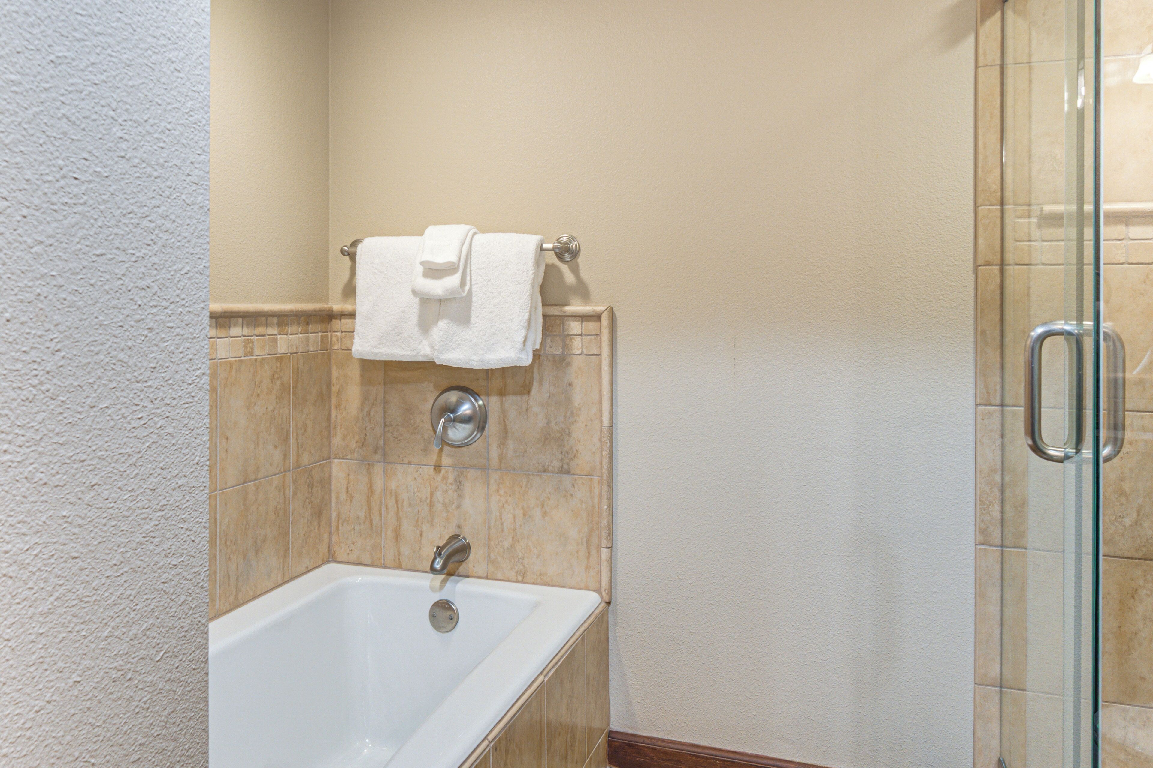 A bathroom with a bathtub, a glass shower enclosure, and a towel rack with two towels.