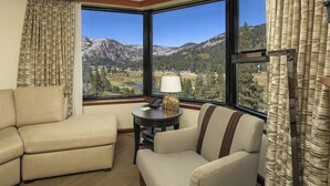 Une chambre d’hôtel dotée d’une grande fenêtre donnant sur les montagnes, d’un canapé, d’un fauteuil et d’une petite table avec une lampe.