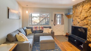 A modern living room with a sectional sofa, ottoman, and a flat-screen TV against a stone wall. - 3 Mi to Slopes! Family-friendly Winter Park Escape (Winter Park)