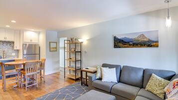 A modern living space with a kitchen, dining area, and a grey sofa with patterned cushions.