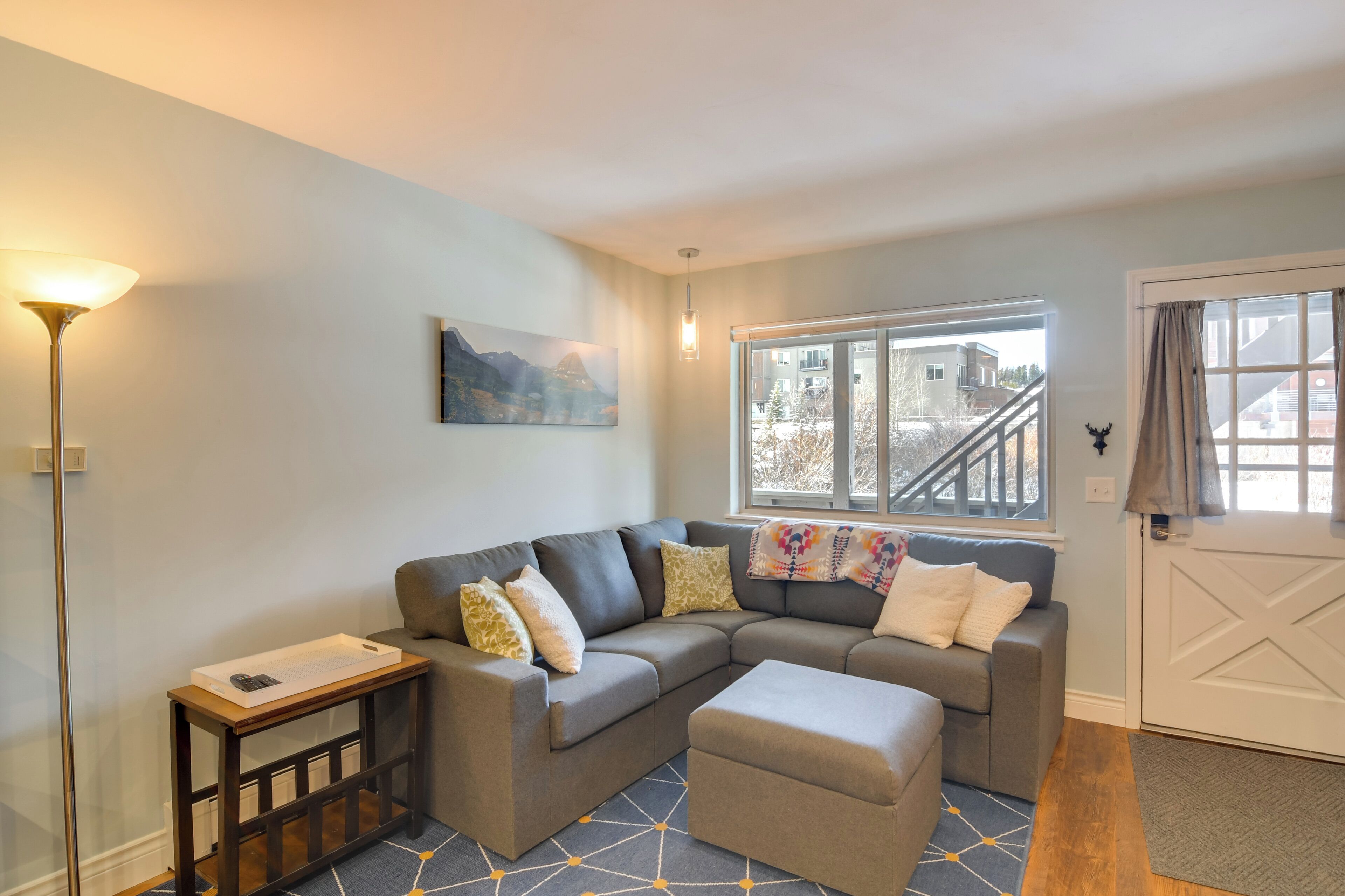 A modern living room with a sectional sofa, a small table, and a large window with a view of a building outside.
