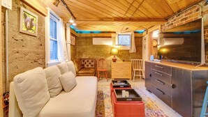 A cozy living room with a sofa, a coffee table, and a TV. There is a wooden ceiling and a brick wall. - Explore CU! Unique Studio w/ Private Courtyard (Boulder)