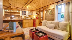 A cozy cabin interior with a wooden ceiling, a kitchen area, a white sofa, and a dining table with a book and a tray. - Explore CU! Unique Studio w/ Private Courtyard (Boulder)