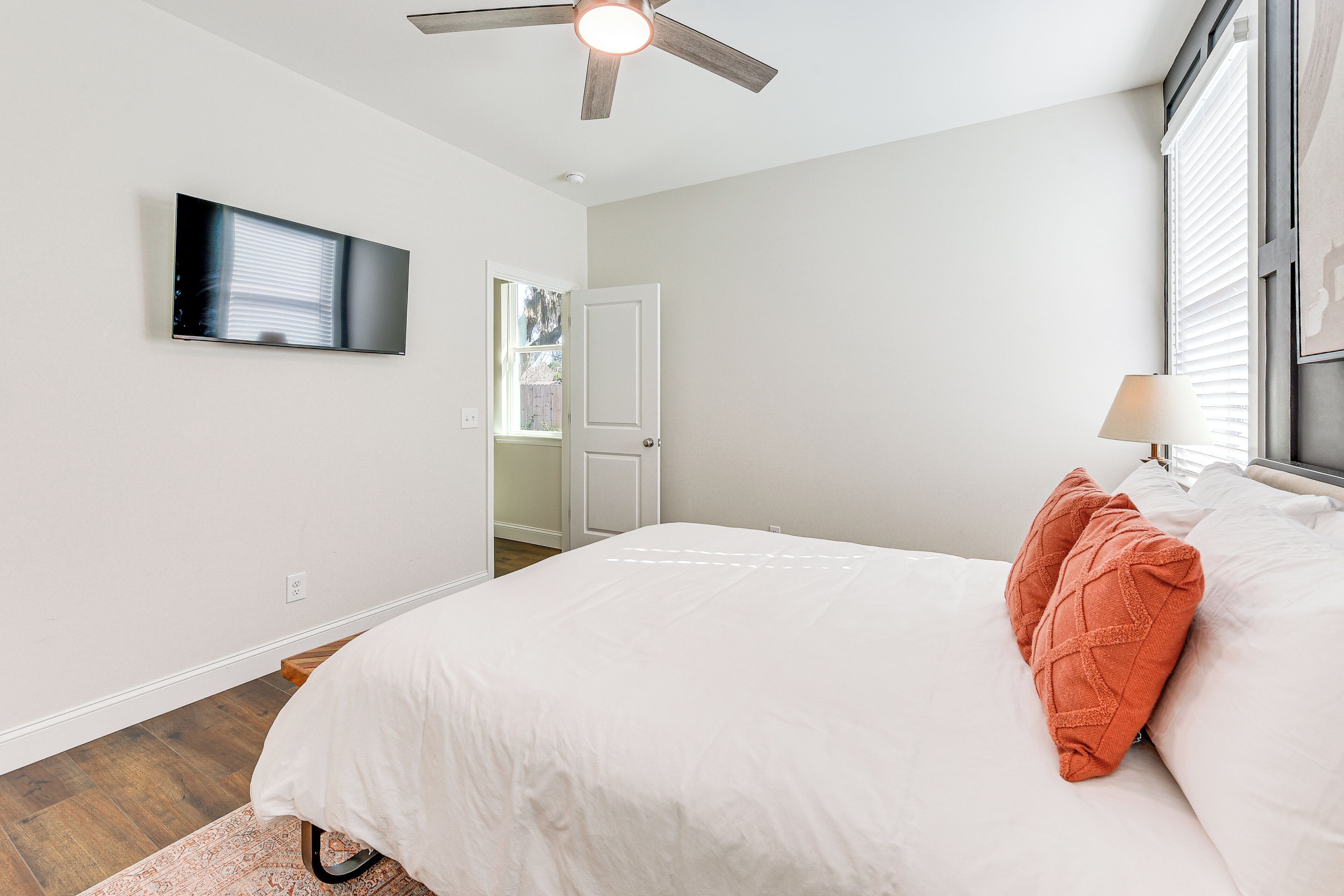 A bedroom with a bed, a ceiling fan, a TV mounted on the wall, and a window with blinds.