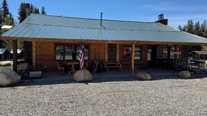 A rustic log cabin with a metal roof, a wooden porch, and a gravel ground.
