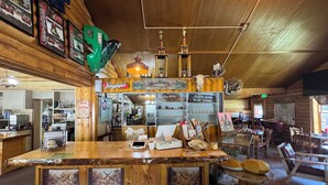 A rustic bar area with wooden walls, framed pictures, and a counter with various items.