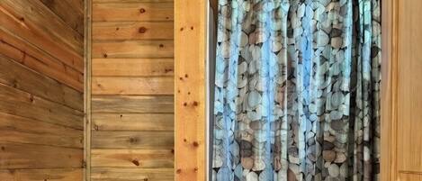Un baño de cabaña de madera con un inodoro blanco, una puerta de madera y una cortina de ducha con estampado de piedras.