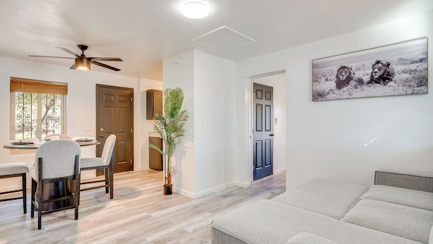 Un soggiorno moderno con un divano grigio, un'area pranzo con tavolo e sedie e una ventola a soffitto.