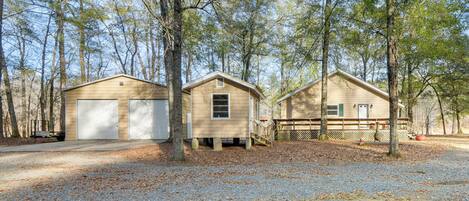 A cabin with a gravel driveway, surrounded by trees.