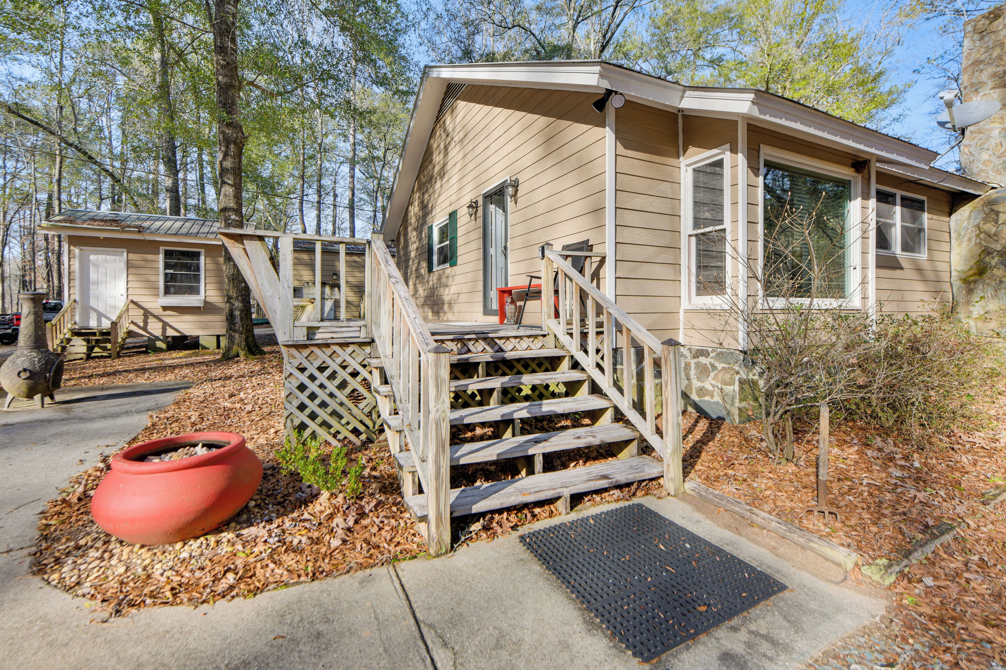 A cabin with a wooden staircase leading to a front door, surrounded by trees and a wooden deck.