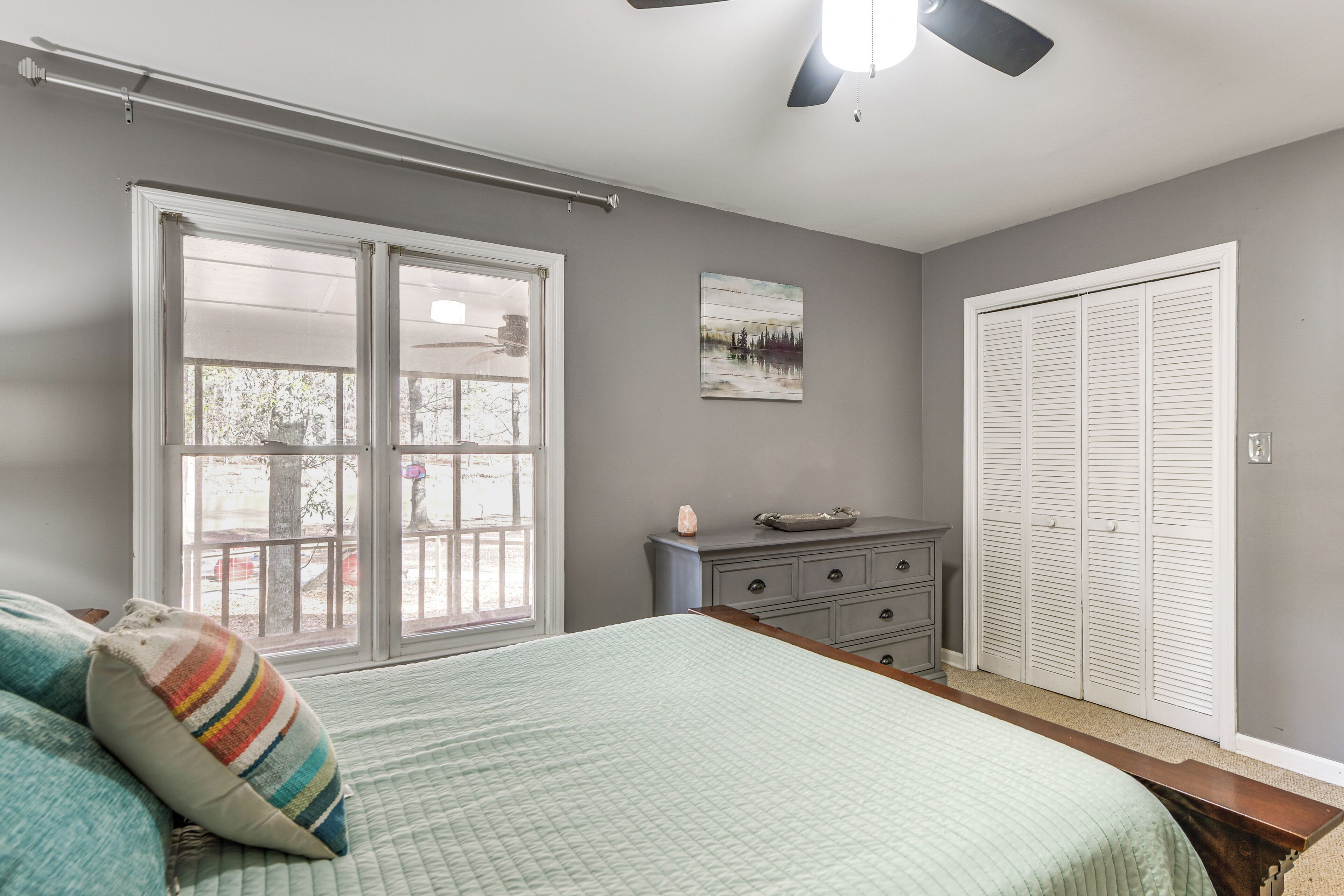 A bedroom with a bed, a dresser, a closet, and a window with a view of trees.