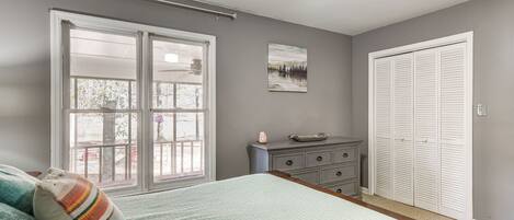 A bedroom with a bed, a dresser, a closet, and a window with a view of trees.