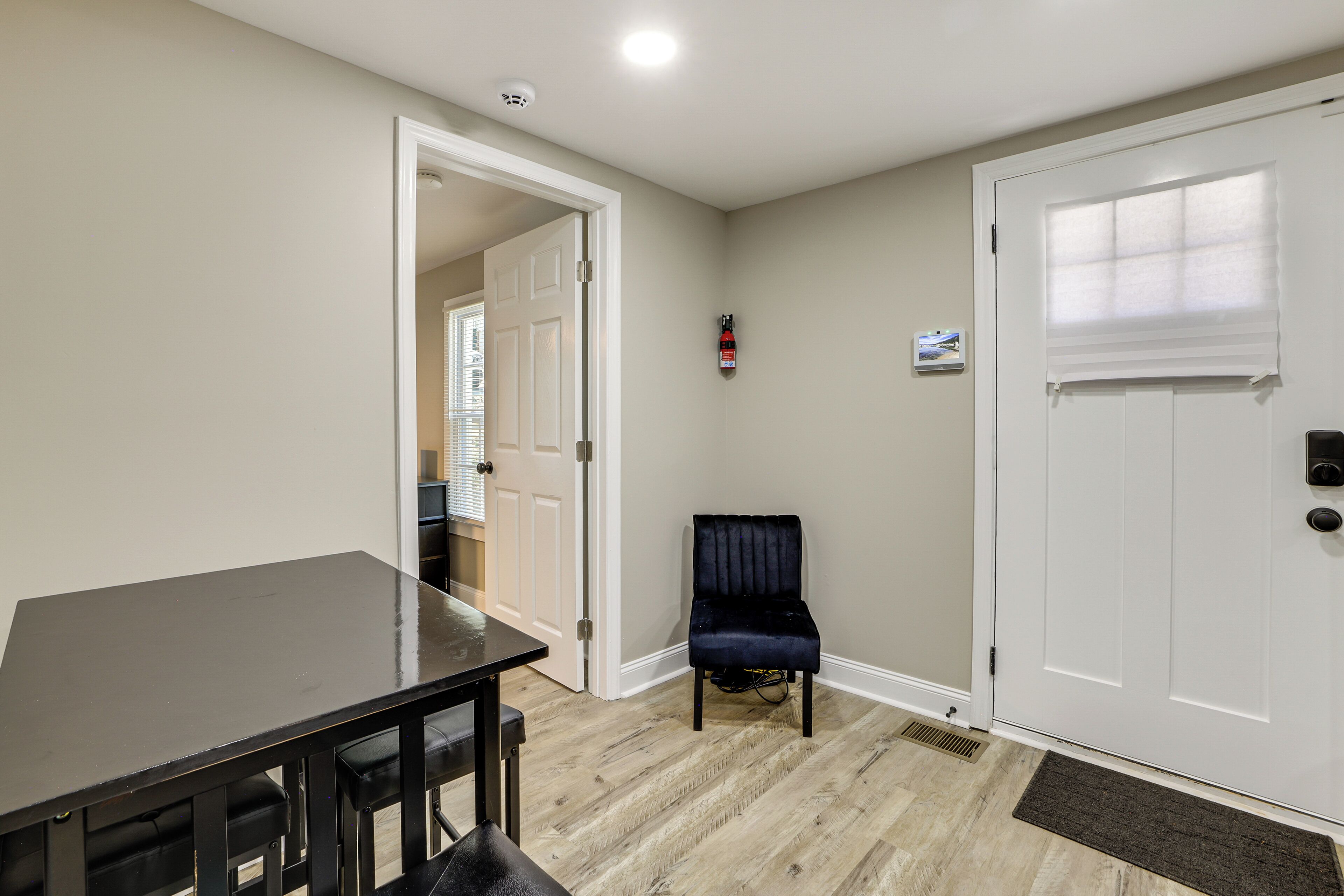 A room with a dining table, a chair, a door, and a fire extinguisher on the wall.