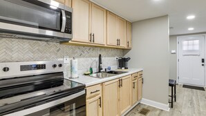 A modern kitchen with stainless steel appliances, wooden cabinets, and a herringbone tile backsplash. - < 3 Mi to Downtown Greenville! Convenient 2BR Home (Greenville)
