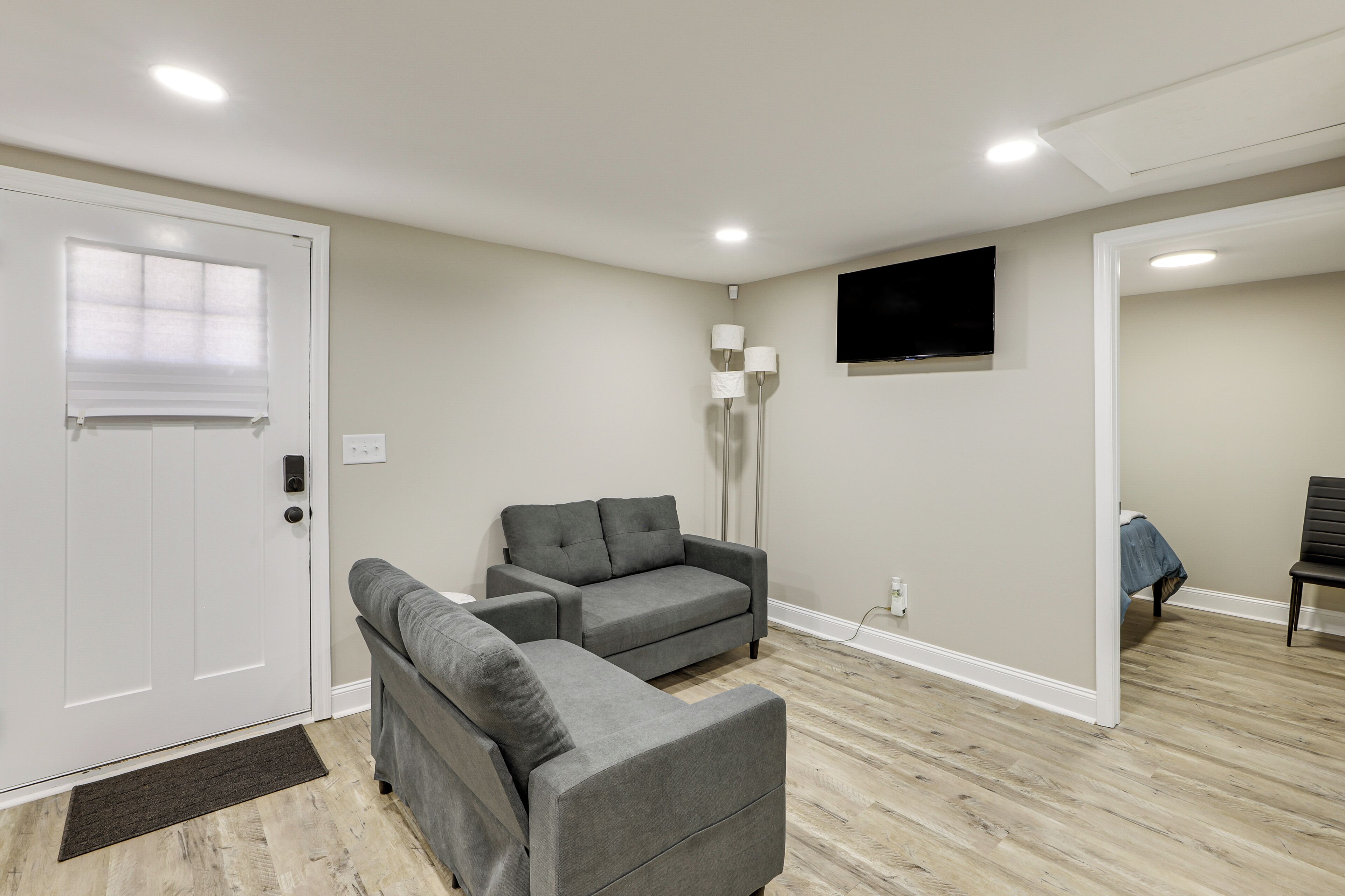 A living room with a grey sofa, a standing lamp, a flat-screen TV, and a wooden floor.