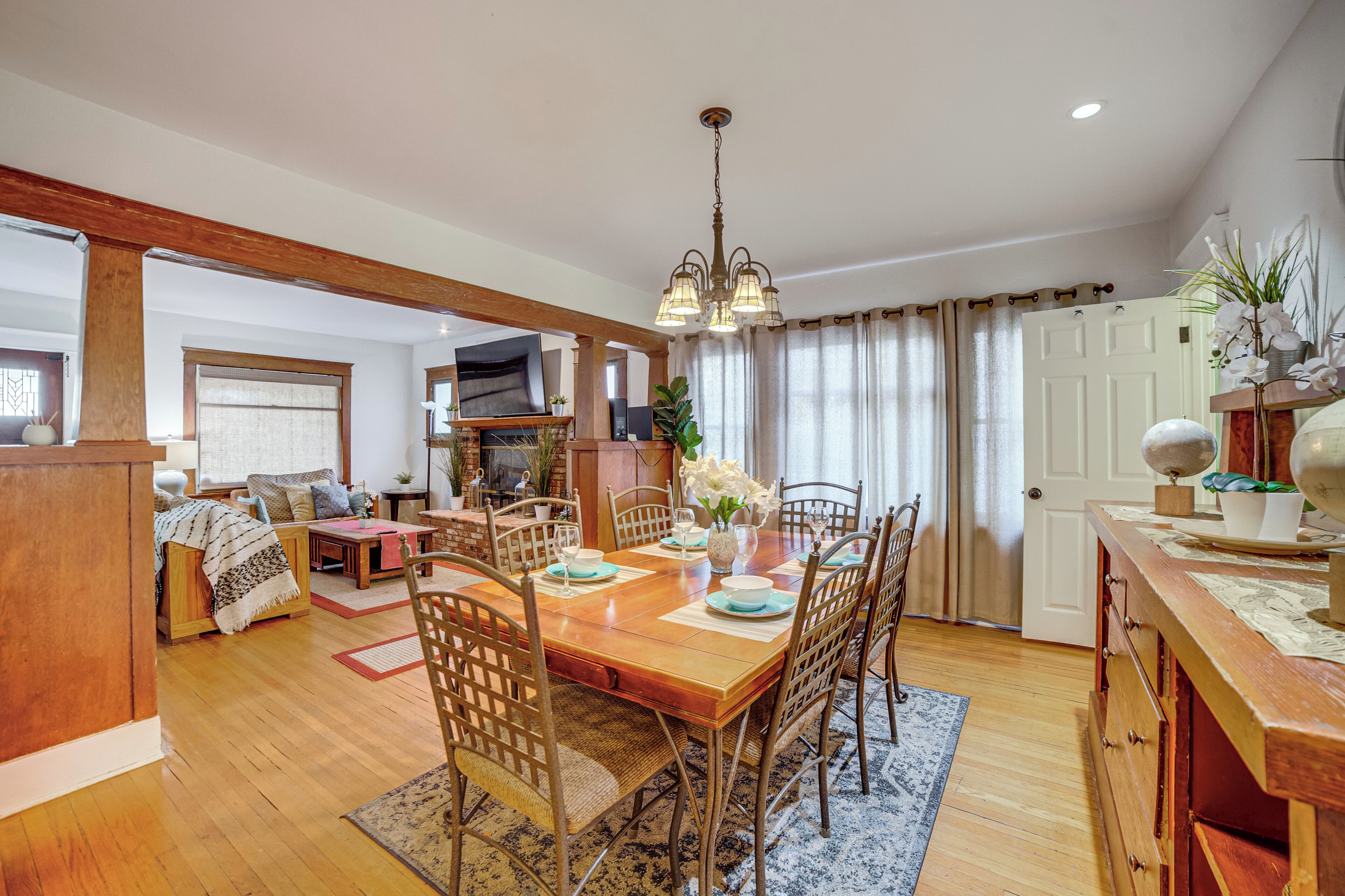A spacious dining area with a wooden table and chairs, a chandelier, and a view of the living room.