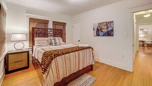 Une chambre à coucher avec un lit, une table de chevet, une lampe, une porte et un tableau au mur.